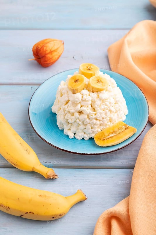 White ?ottage cheese, Curd, with Banana on blue wooden background and orange textile, side view, close up