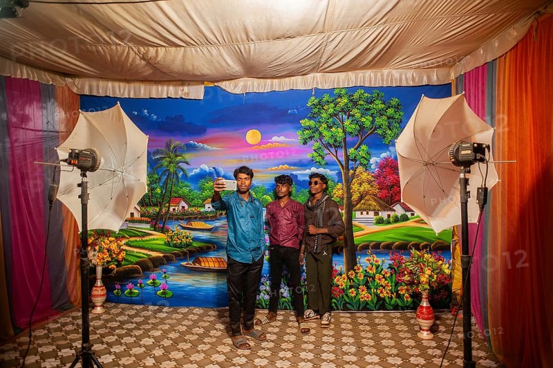 Three teenagers are taking pictures of themselves in an itinerant photo studio. Photographed in tribal India (Bastar region, India) . They are using a smartphone