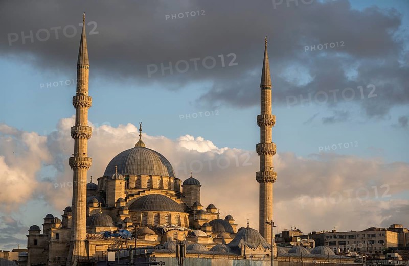 Majestic view of a historical mosque in Istanbul, captured under a glowing sky at sunset. The architectural grandeur and cultural significance of the mosque stand out against the dramatic backdrop