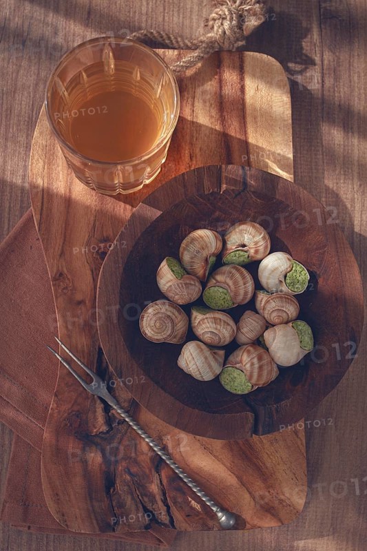 Snails cooked with herb oil on a wooden plate, served with white wine, natural light, no people
