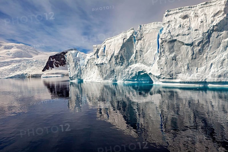 Large iceberg with clear reflection in front of mountain landscape and cloudy sky, icebergs in the landscape of the Southern Ocean in Antarctica