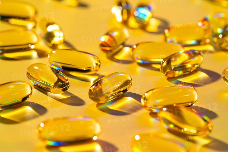 Golden softgel capsules spread across a vibrant yellow surface, showcasing a health supplement rich in essential vitamins. Ideal for maintaining a balanced and nutritious lifestyle