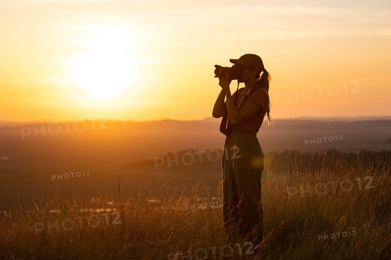 Young woman taking pictures at sunset, standing in tall grass, landscape, view of Lake Victoria and Mabamba swamp, Lake Victoria, Uganda
