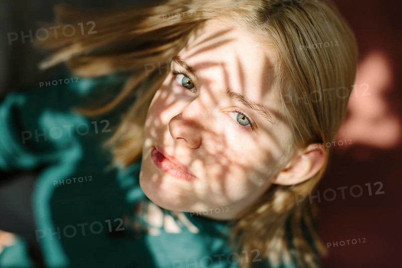 A captivating portrait of a teenager with sunlit shadows creating patterns on their face, producing an artistic and introspective mood. The light accentuates their thoughtful expression