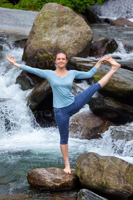 Yoga outdoors, woman doing Ashtanga Vinyasa Yoga balance asana Utthita Hasta Padangushthasana, Extended Hand-To-Big-Toe Pose position posture outdoors at waterfall