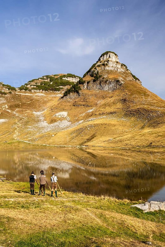 The Austrian alphorn trio Klangholz plays the alphorn at Lake Augstsee on Mount Loser. Mount Atterkogel in the background. Autumn, good weather, blue sky. Reflection. Altaussee, Bad Aussee, Ausseer Land, Totes Gebirge, Styria, Upper Austria, Austria