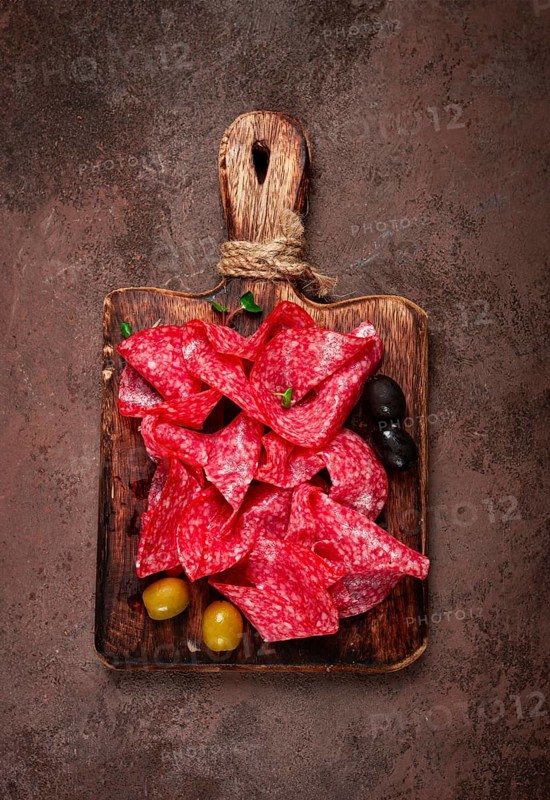 Sliced salami sausage, on a wooden chopping board, decorated with olives and herbs, close-up, no people