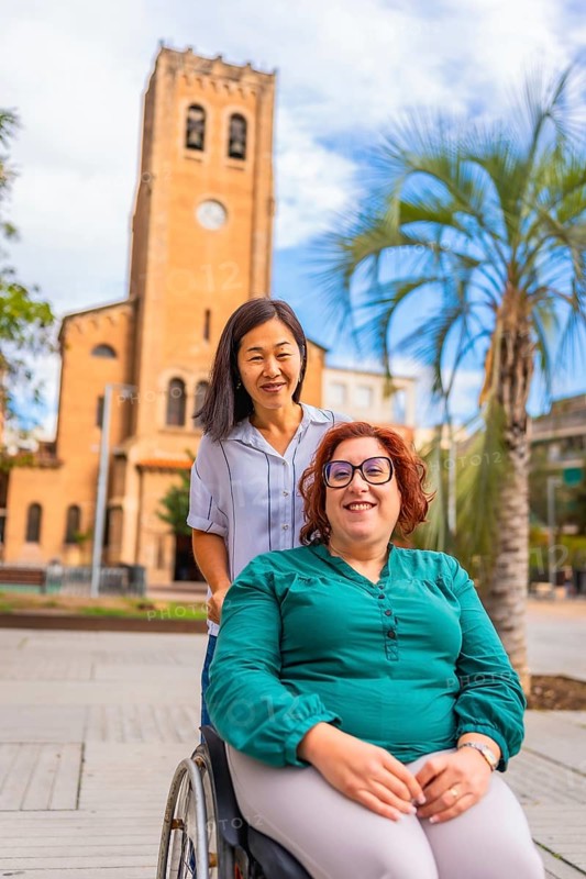 Asian woman pushing the wheelchair of a friend along downtown in the city