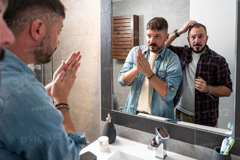 A gay couple stands together in front of a bathroom mirror, engaging in their morning routine. They appear relaxed and comfortable, embodying a sense of companionship and care