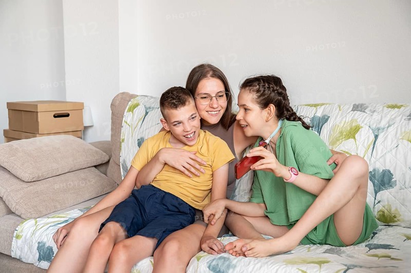 A loving family shares a joyful moment with phone on the couch. A girl with a tracheostomy and a boy with cerebral palsy enjoy the closeness and warmth of their togetherness