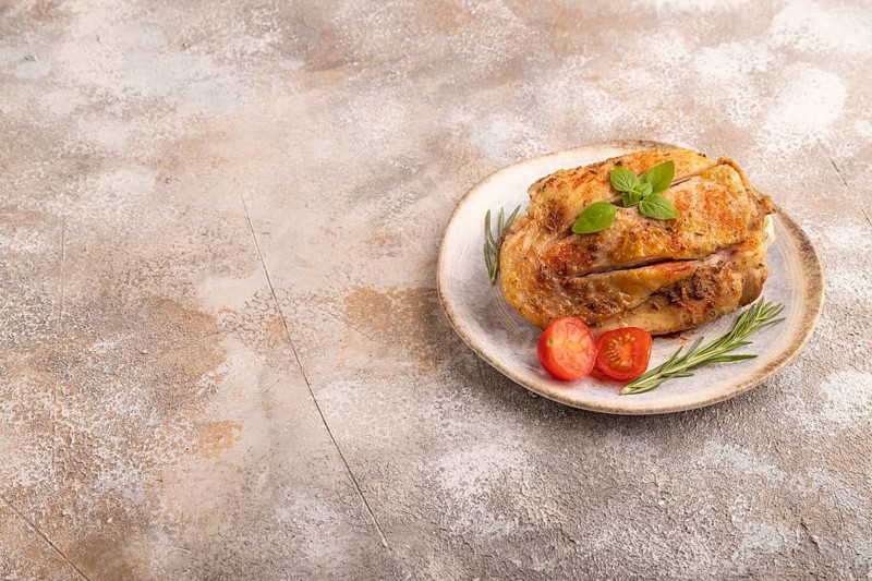 Fried Turkey Thigh with spices and rosemary on plate on brown concrete background. side view, copy space