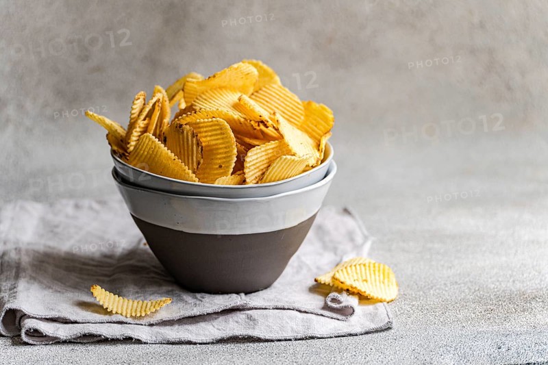 A bowl of delicious homemade potato chips, perfectly golden and crispy, sits on a neutral gray surface. The textured ceramic bowl adds a rustic charm to this tasty snack