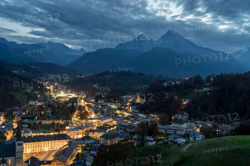 Berchtesgaden glows with warm lights against the dark silhouette of the Watzmann mountain This captivating nighttime view showcases the serene beauty of the Bavarian Alps under dramatic skies