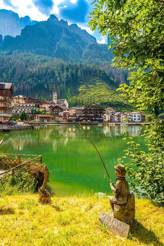 Wooden statue of a fisherman with a fishing rod sitting by the alleghe lake with the civetta mountain in the background, in the dolomites, italy