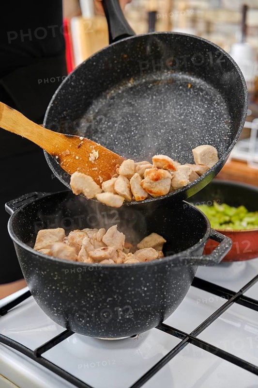 Fried chicken pieces are transferred to a pan for further cooking
