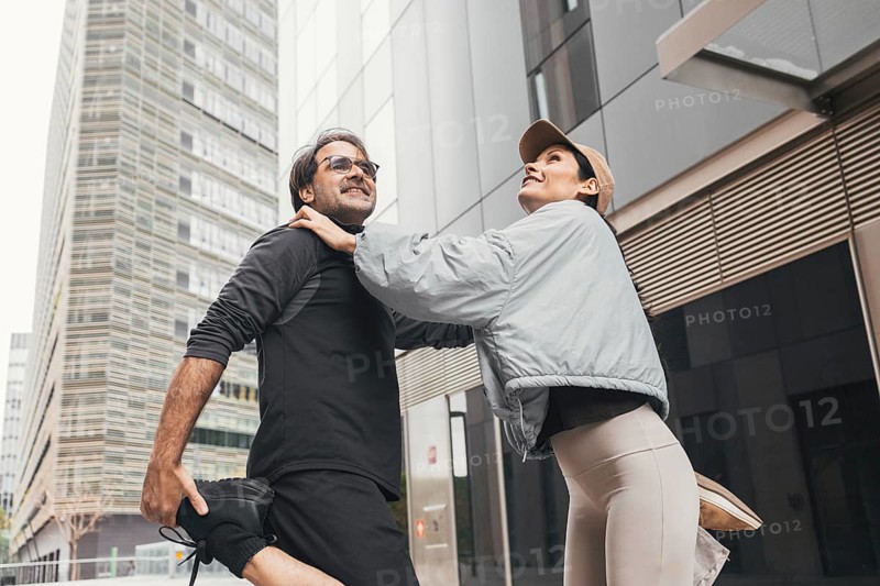 A fit couple enjoys a stretching session together in an urban environment. Their activewear highlights their commitment to fitness and a healthy lifestyle amidst the city backdrop