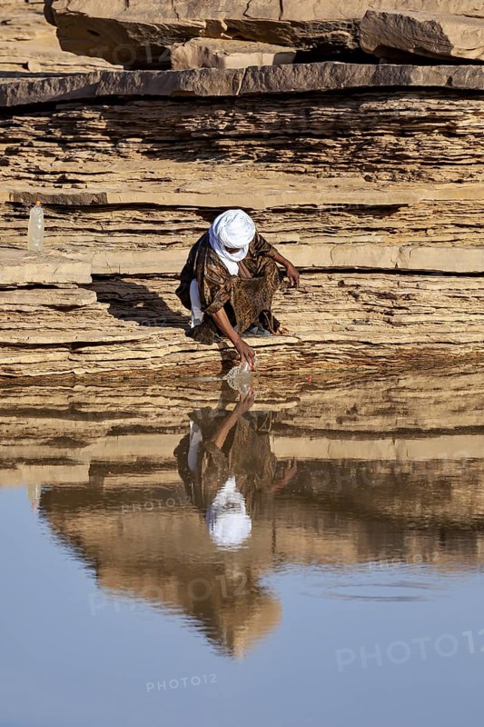 A person draws water from a rock in a desert-like environment, Tuareg collecting water in the Sahara in Algeria