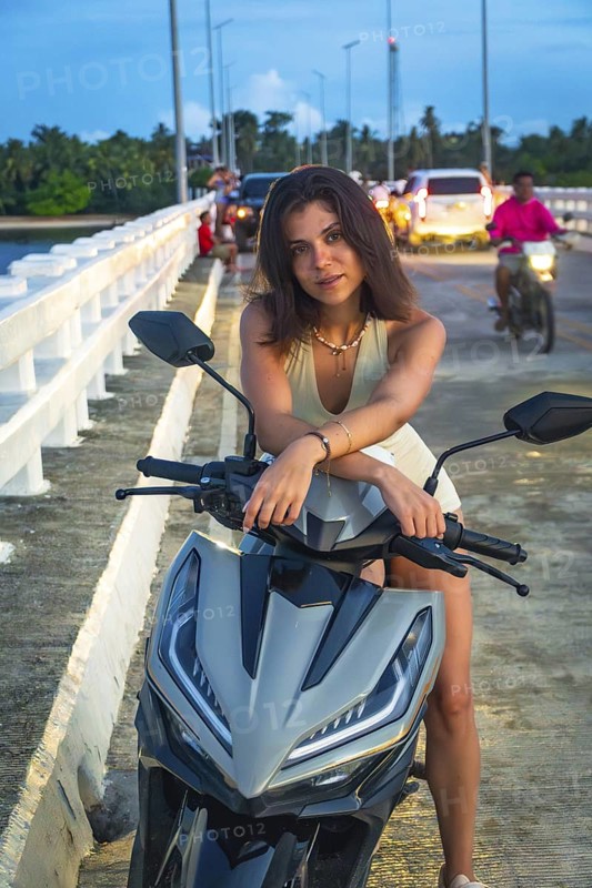 Tourist enjoying her scooter on afam bridge, siargao island, philippines, during a tropical sunset