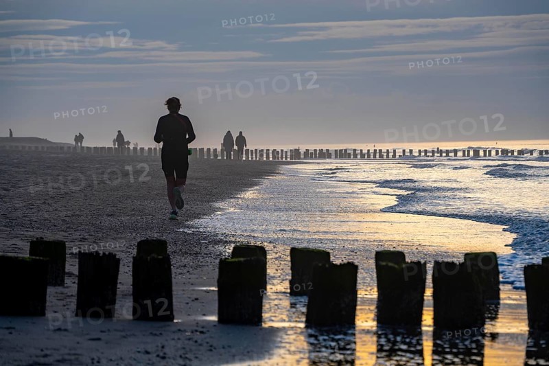 Winter on the North Sea, sunset at the beach, joggers, beach walkers, coastal protection, through wooden posts, paalhoofden, on the beach, breakwater, piles rammed into the sandy soil in double rows slow down the waves and ocean currents and thus slow down the flow rate of seawater, so less sand is washed away from the standing position, near Domburg, Walcheren peninsula in the Dutch province of Zeeland