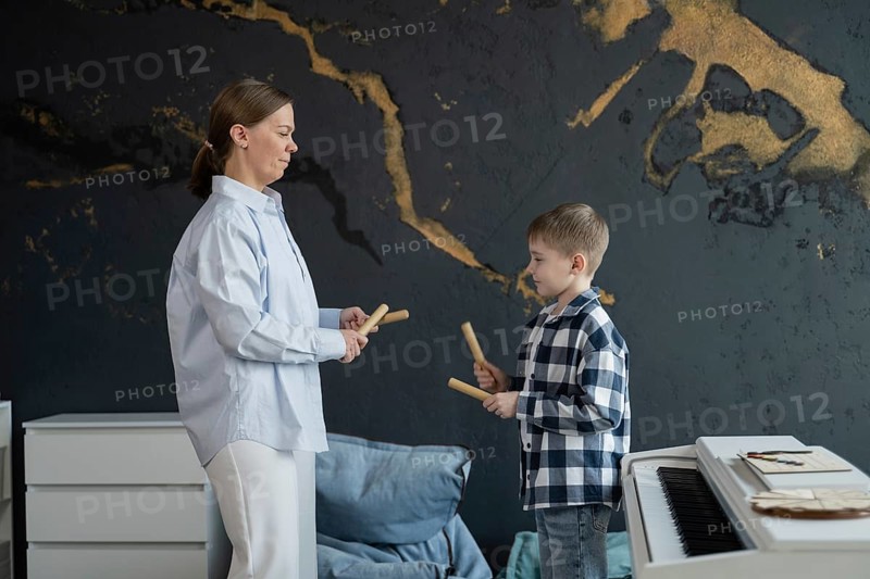 A teacher is guiding a young student in a music lesson inside a stylish studio. The piano in the foreground suggests the exploration of musical instruments