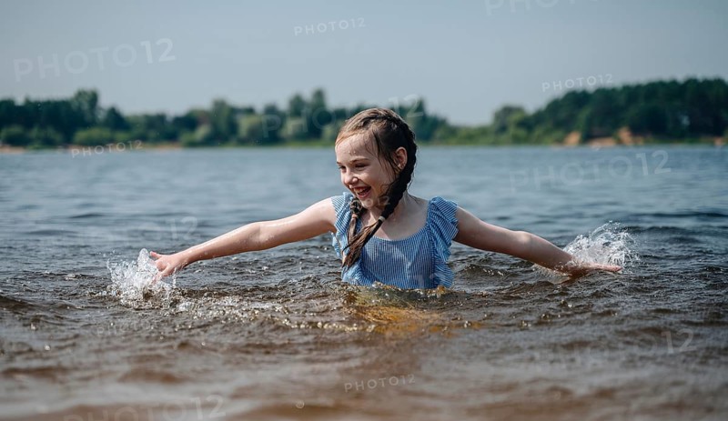 A cheerful young girl splashes playfully in the water, enjoying a sunny day outdoors. Her happiness is contagious, captured in a moment of pure summer joy
