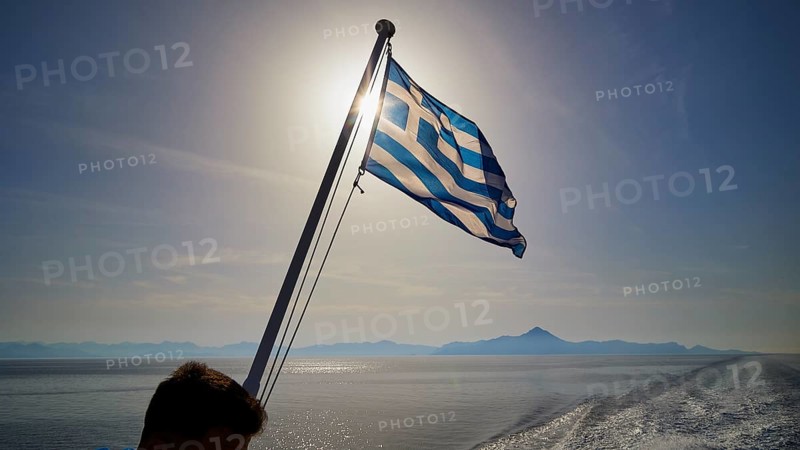 Greek flag waving in the wind, over the sea in sunny weather, crossing Rhodes to Symi, ferry, Symi, Dodecanese, Greek Islands, Greece