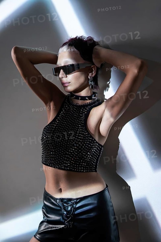 A woman embodies cyberpunk fashion with striking metallic accessories, futuristic sunglasses, and edgy attire. Her pose and outfit exude vibrant, avant-garde style