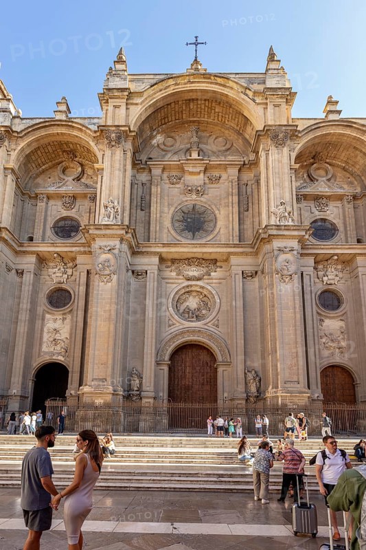 Magnificent baroque cathedral façade with people in front of it under a blue sky, Granada