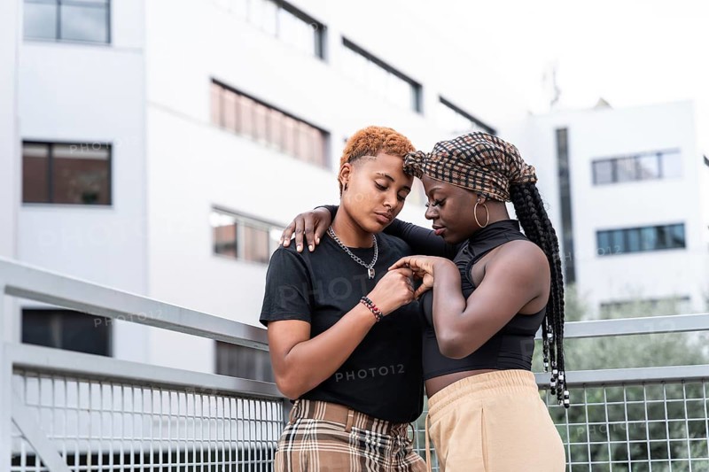 A loving LGBT multiethnic couple shares a tender embrace outdoors against a modern architectural background, capturing warmth and affection in the vibrant city setting