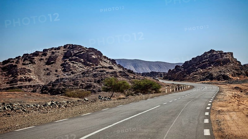 Lonely road between rocky desert hills under a clear blue sky, roads through the Sahara in Algeria