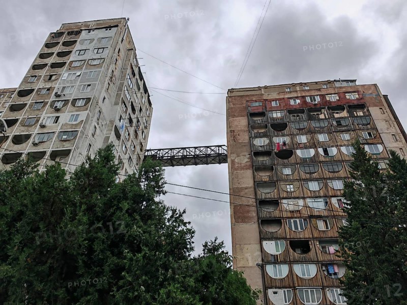 Two tall residential buildings with a bridge as a connection in a dramatic atmosphere in a wooded urban landscape, Tbilisi, Georgia