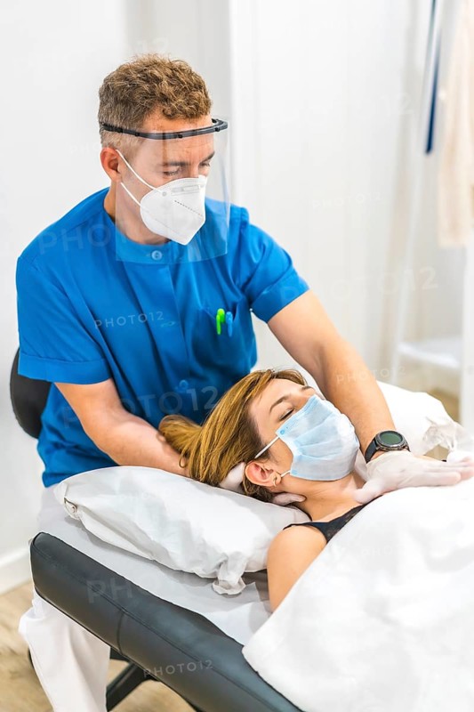 Structural osteopathy of a physiotherapist with protective measures for a patient on the stretcher. Covid-19 pandemic. Osteopathy, therapeutic chiromassage