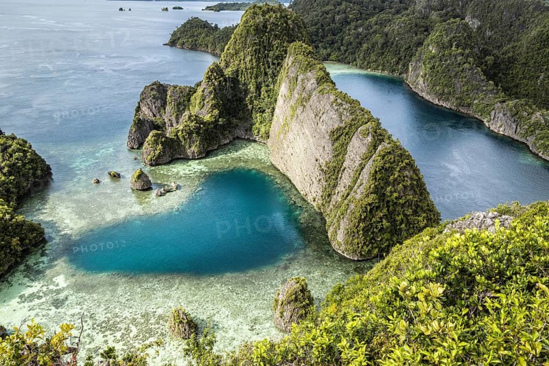 From above, a drone captures the breathtaking Raja Ampat Archipelago in Indonesia. The image shows vivid turquoise waters intertwining with lush, verdant cliffs and islands, highlighting the pristine beauty of this remote paradise