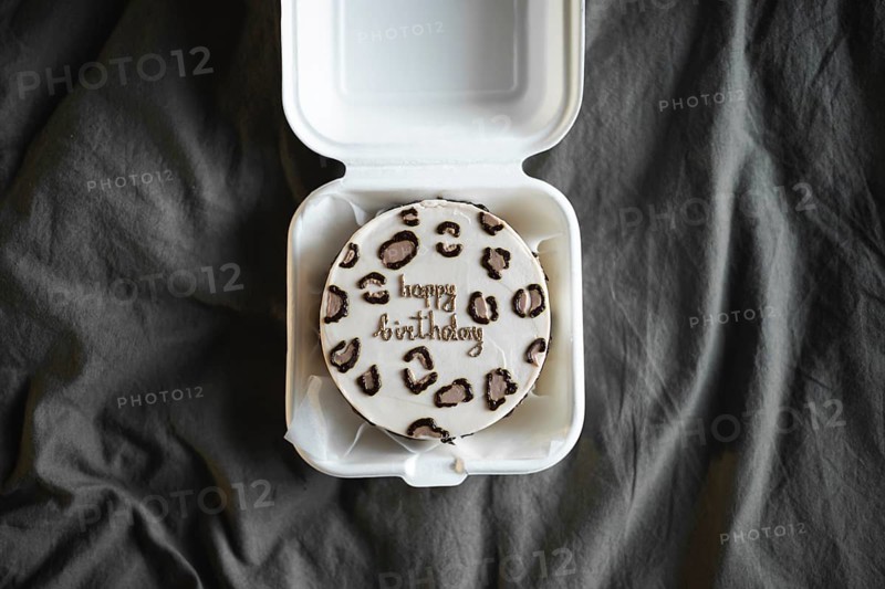 Top view of a bento birthday cake with happy birthday lettering in a white takeout box, set against a textured grey backdrop