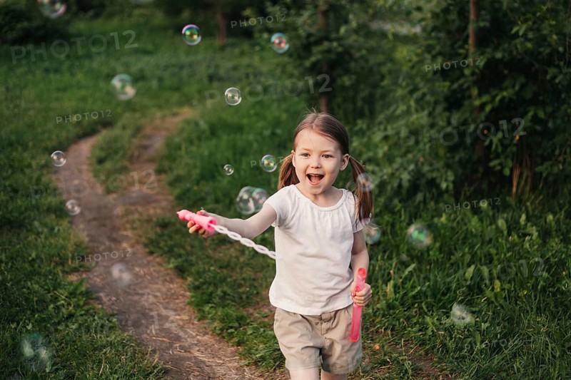 A joyful girl embraces summer play, running through a lush green garden while blowing and chasing sparkling soap bubbles, capturing the essence of childhood happiness and fun