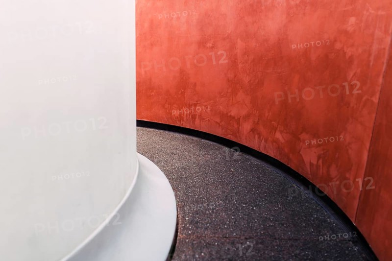 An eye-catching minimalist architectural detail featuring a smooth white column juxtaposed with a vibrant red textured wall, highlighting the beauty in simplicity and form