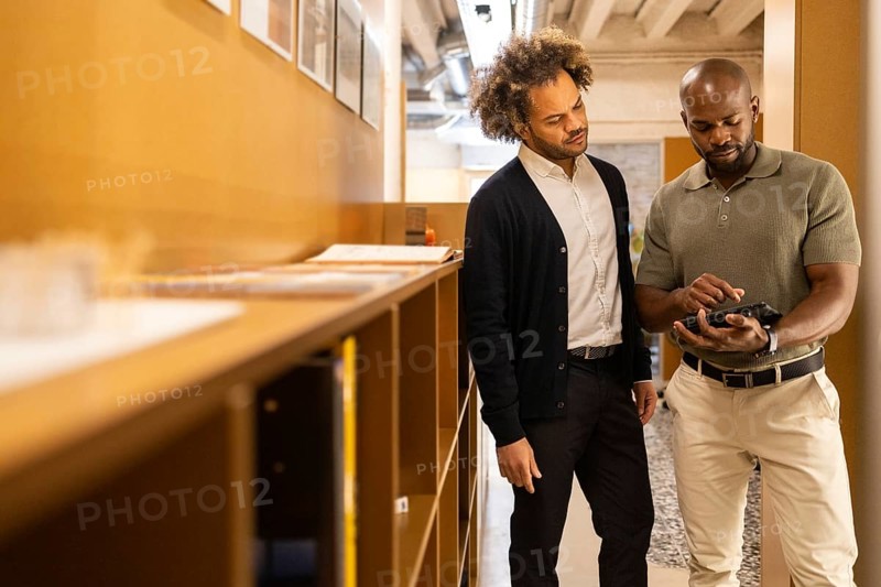 Two professionals collaborate in a modern coworking space in Barcelona, engaging in a discussion while reviewing information on a digital tablet amidst a productive atmosphere