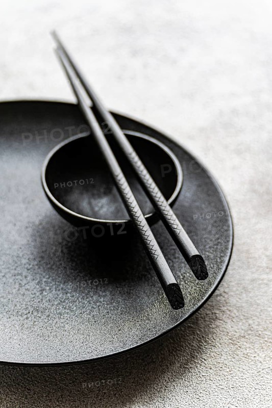 Minimalist black table setting featuring a textured plate, small bowl, and detailed chopsticks. The monochrome design offers a sleek and sophisticated dining aesthetic