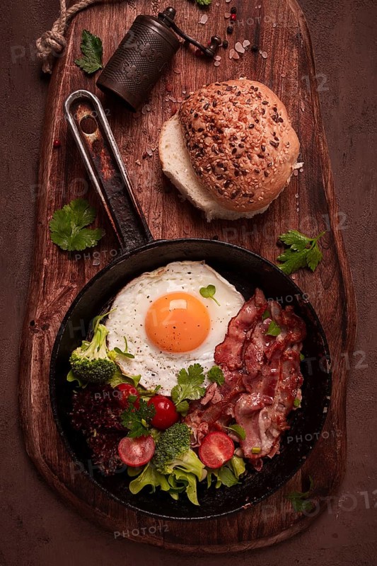 Fried egg, with bacon and vegetables, in a cast-iron frying pan, top view, homemade breakfast