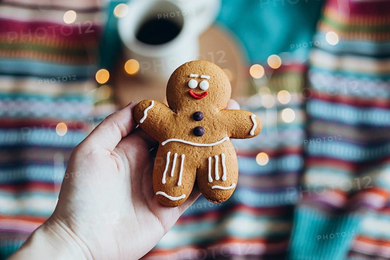 A close-up of a charming gingerbread man cookie held in hand, showcasing intricate icing details, with a colorful, festive background, coffee and warm lighting