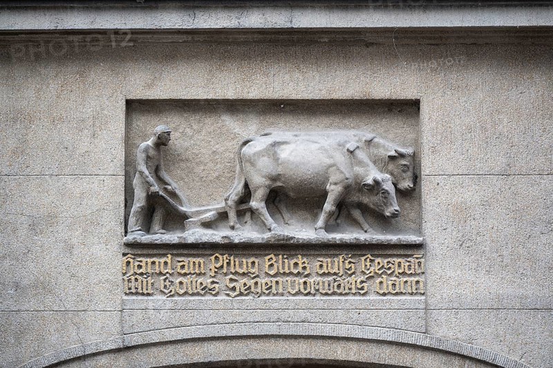 Stone relief depicting a farmer using oxen for ploughing, including a saying in fracture script that urges hard work and trust in God, the motif symbolizes traditional agriculture and work ethics of the past, Constance, district of Constance, Baden-Württemberg, Germany