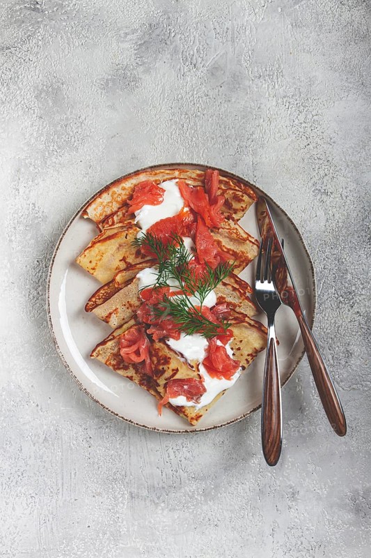 Delicious pancakes with salmon and sour cream, breakfast, on a plate, rustic style, with cutlery
