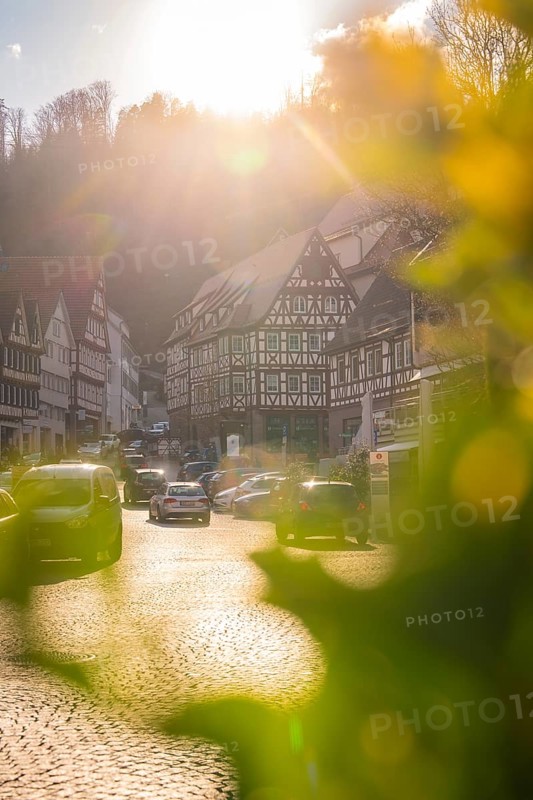 Sunlight over half-timbered houses in a village with cars on the street, Calw in spring, Black Forest, Germany