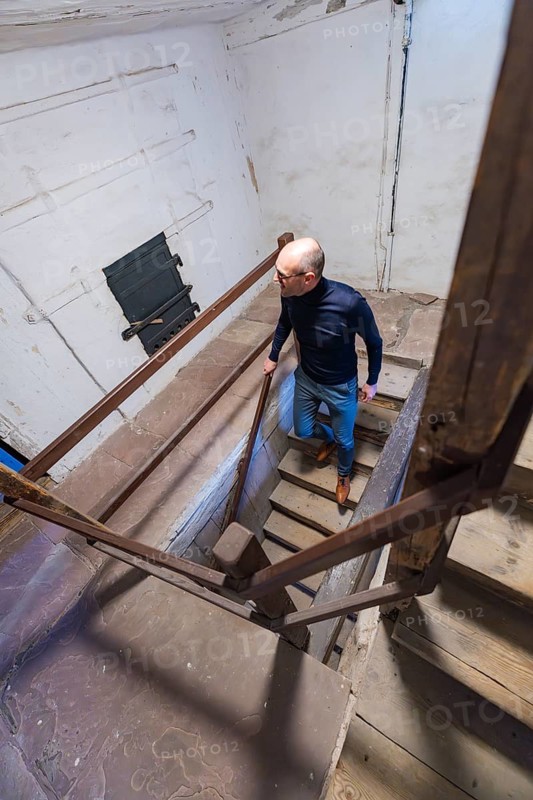 A man climbs a wooden staircase in an old building, illuminated from above, Prison Museum, Der Lange, Calw, Black Forest, Germany