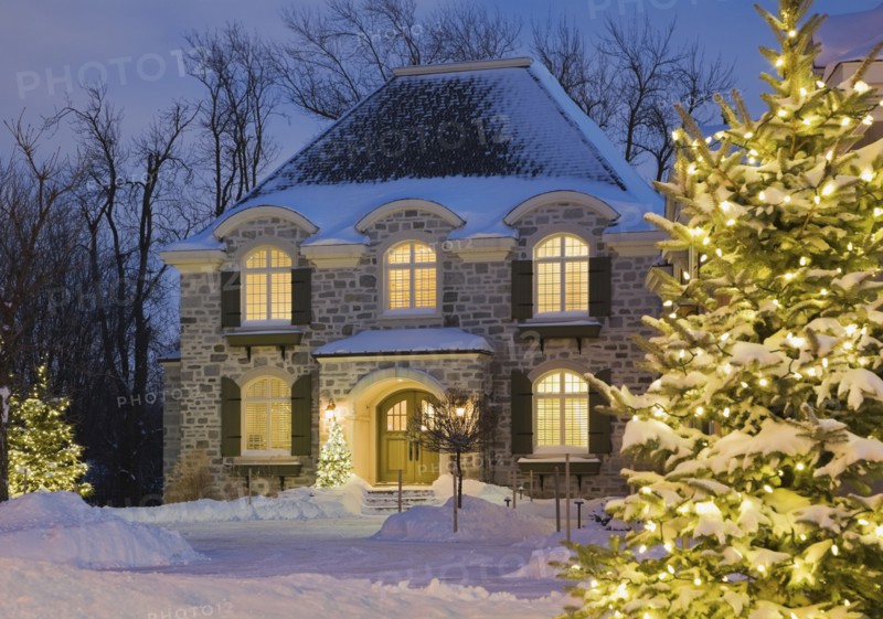 Luxurious residential cottage style home with illuminated evergreen trees at dusk in winter, Quebec, Canada