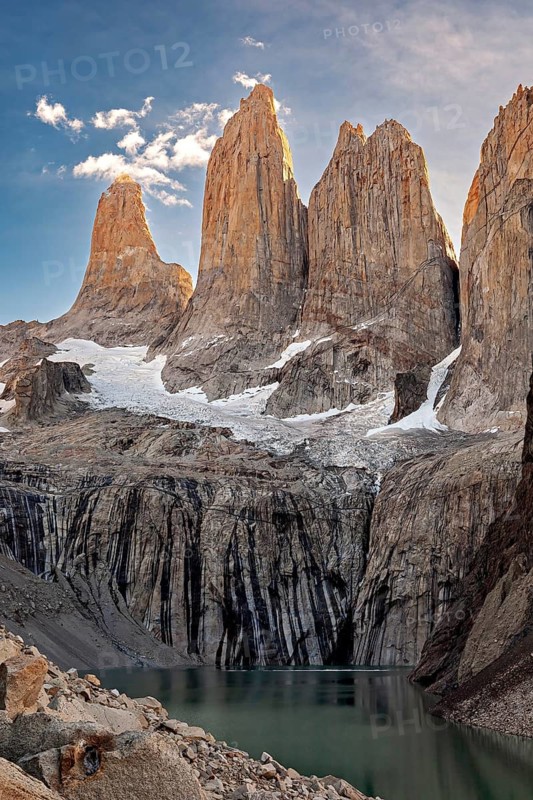 High, sunlit cliffs towering over a calm lake with a clear sky, The rock towers of Torres del Paine in Patagonia Chile