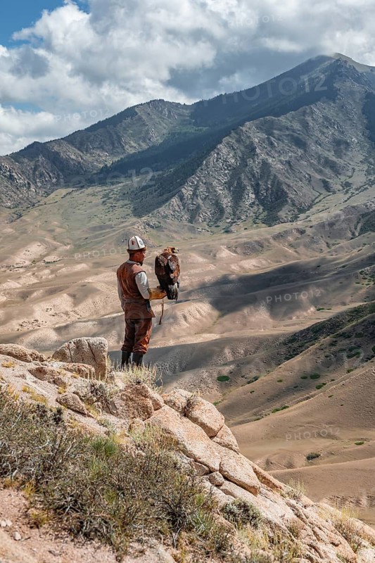 Traditional Kyrgyz eagle hunter hunting in the mountains in a dry landscape, near Kysyl-Suu, Issyk Kul, Kyrgyzstan