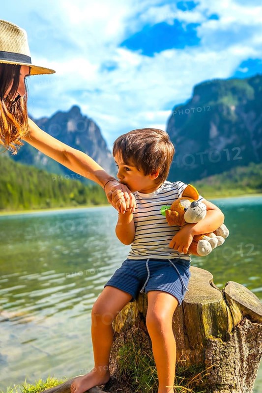 Mother gently holding hands with her son, sitting on a tree stump by a serene lake surrounded by the stunning dolomites in italy