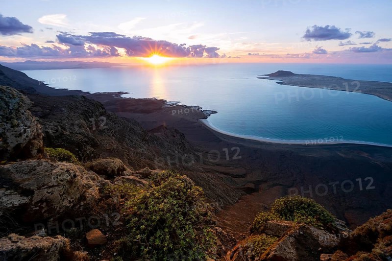 View from steep cliffs to sea and coast with sun stars, Mirador del Porrito viewpoint at sunset, Lanzarote, Canary Islands, Spain