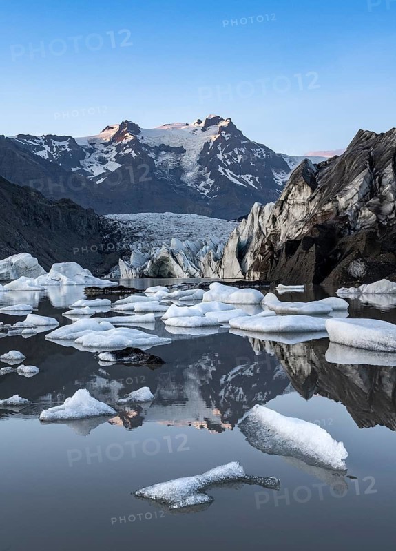 Reflection in the Svínafellslon glacier lagoon with ice floes, Svínasfellsjökull glacier tongue, glaciated mountain peak Hrútfjallstindar in the background, at sunset, Svínafell, Iceland